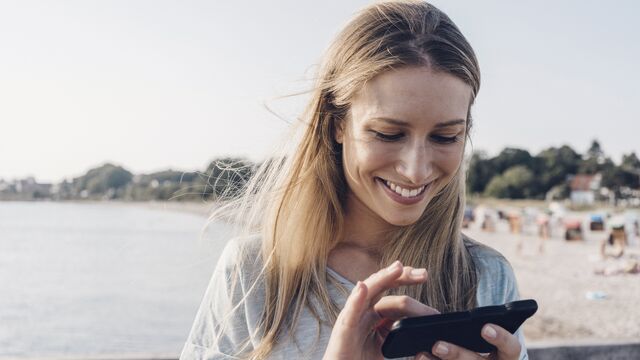 Ung dame med mobil på strand